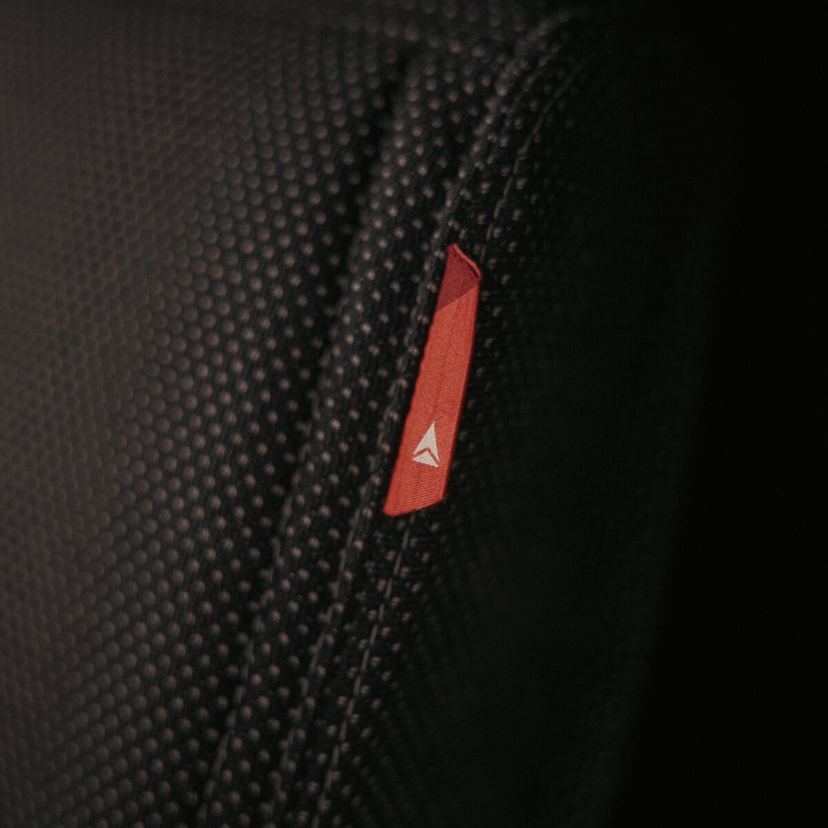 Close-up of a textured black seat surface featuring a small red Delta-branded fabric tag.
