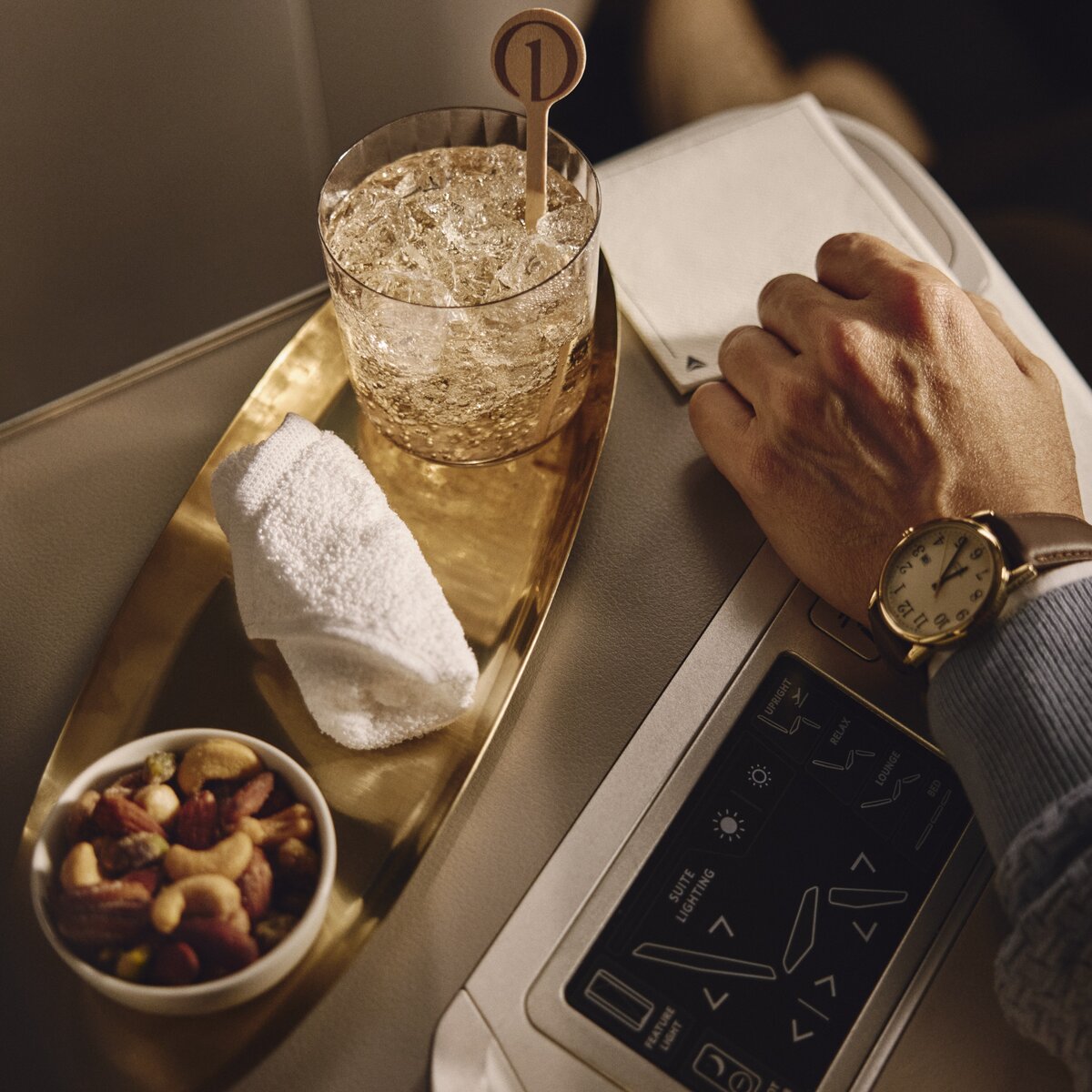 Passenger enjoys a welcome beverage and mixed nuts beside Delta One seat controls.