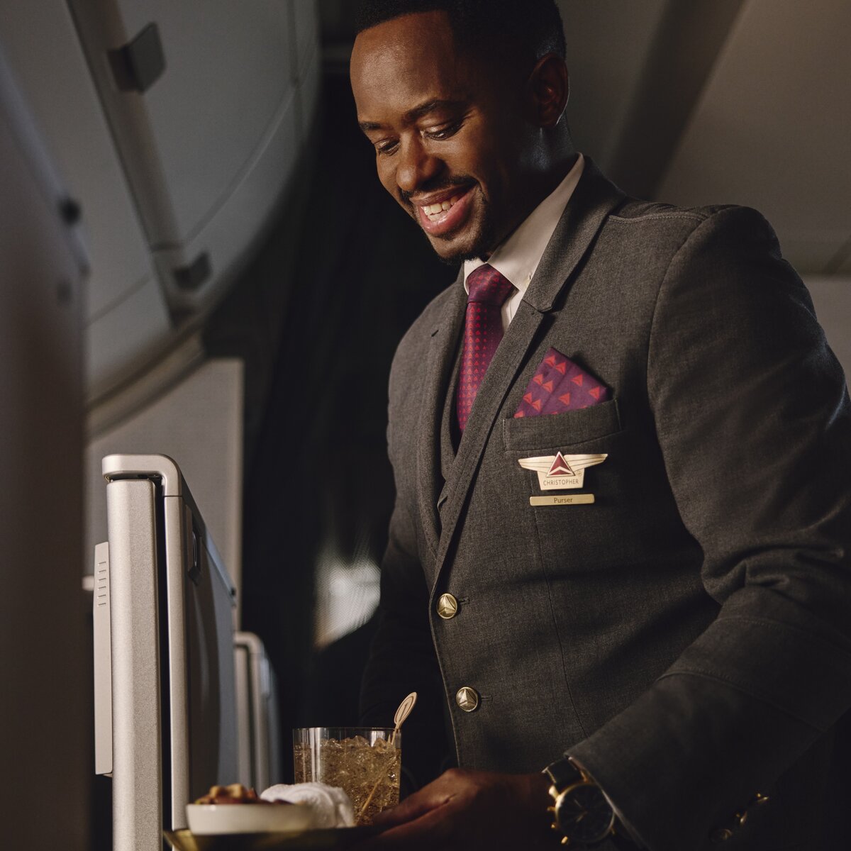 Flight attendant presents a welcome drink and snack service in the Delta One cabin.