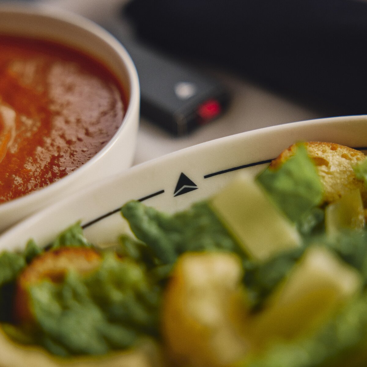 Bowl of tomato soup served alongside a fresh green salad with croutons on an airline meal tray.