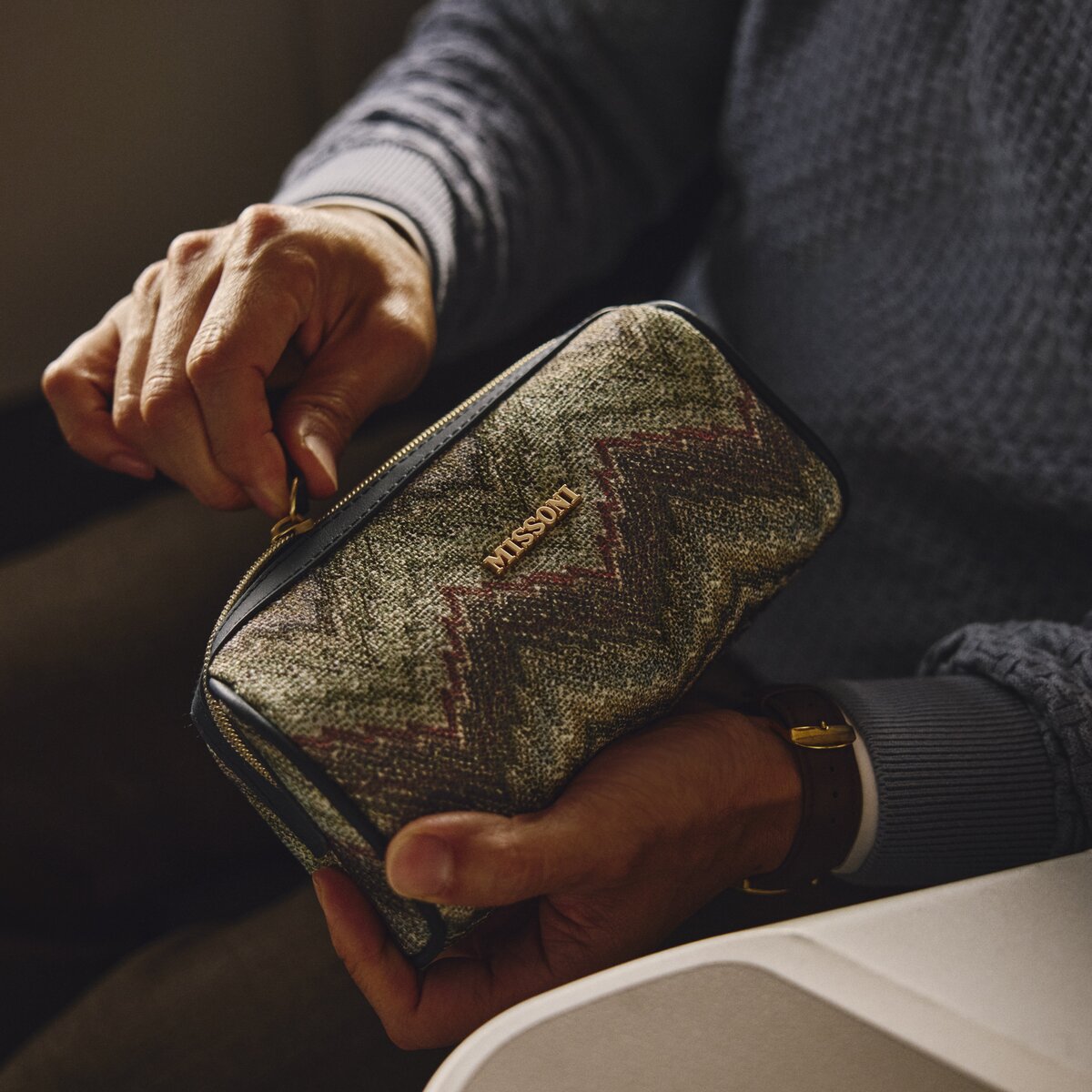 Hands opening a patterned travel amenity kit while seated in a premium airline cabin.
