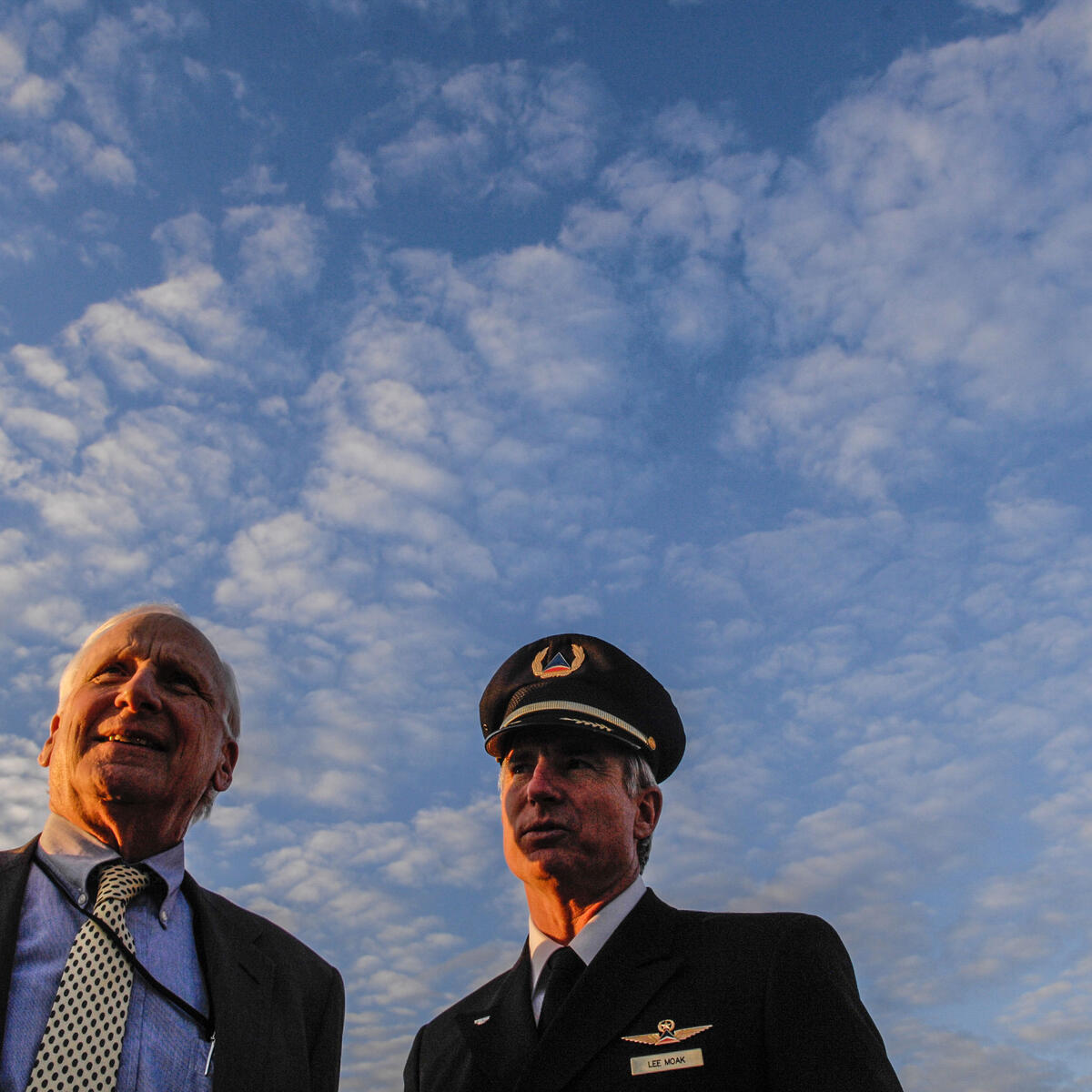 Former Delta CEO Jerry Grinstein stands with a Delta pilot against a blue, cloudy sky.