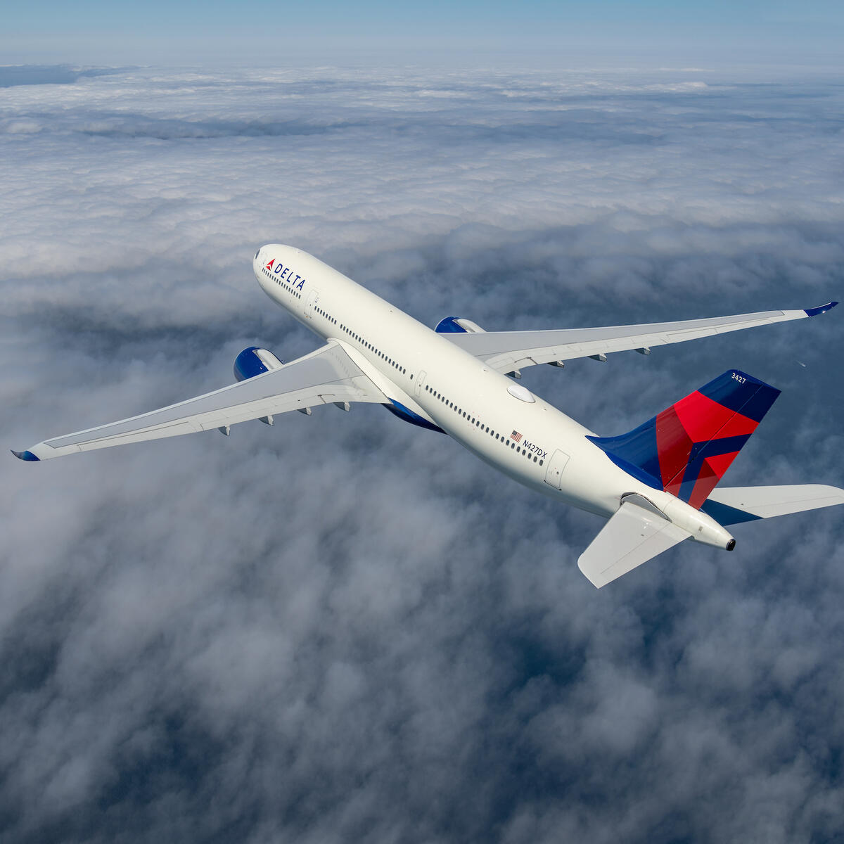 A Delta Air Lines A330-900 flies over clouds.
