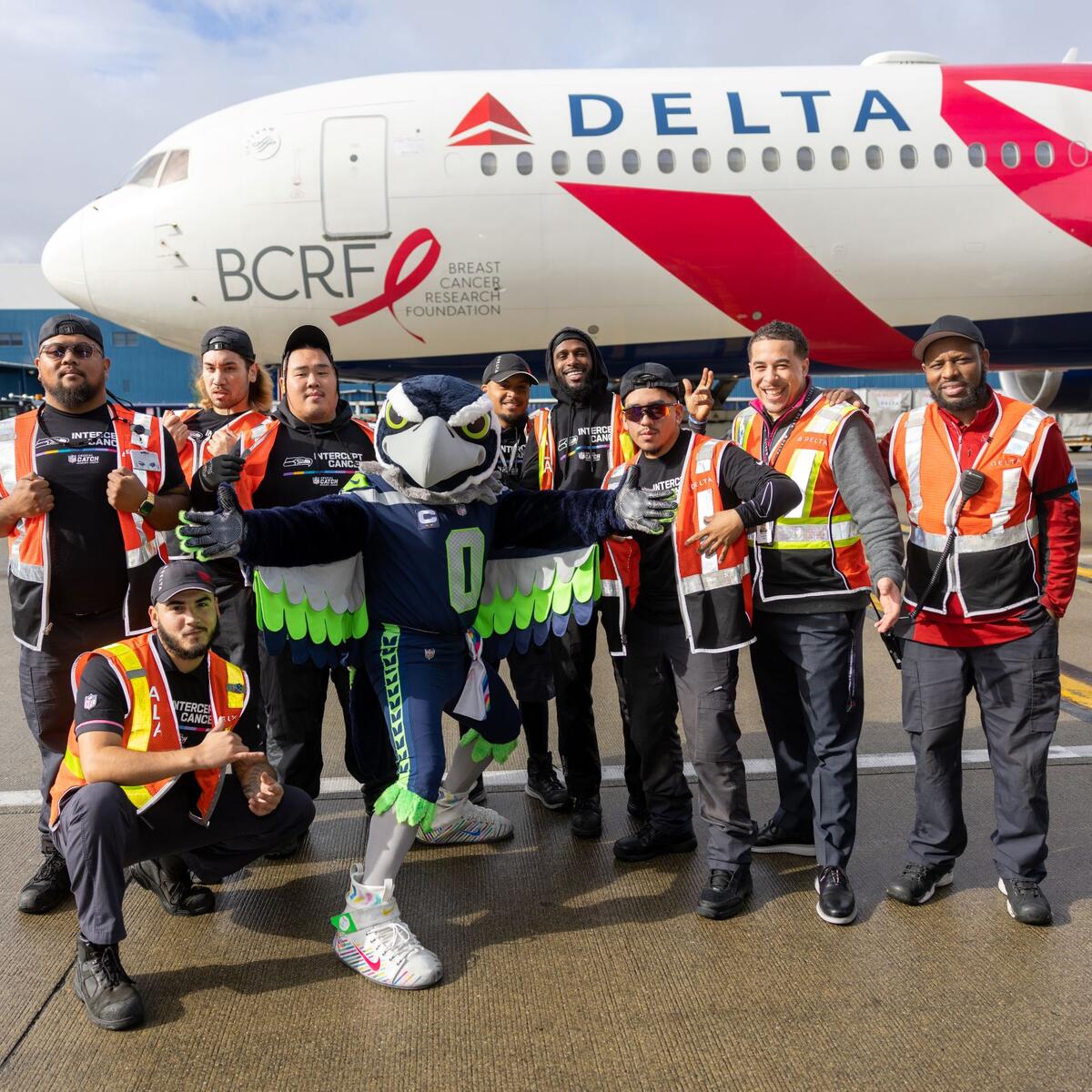Delta ground crew members pose in front of the airline's "Pink Plane" with the Seattle Seahawks mascot.