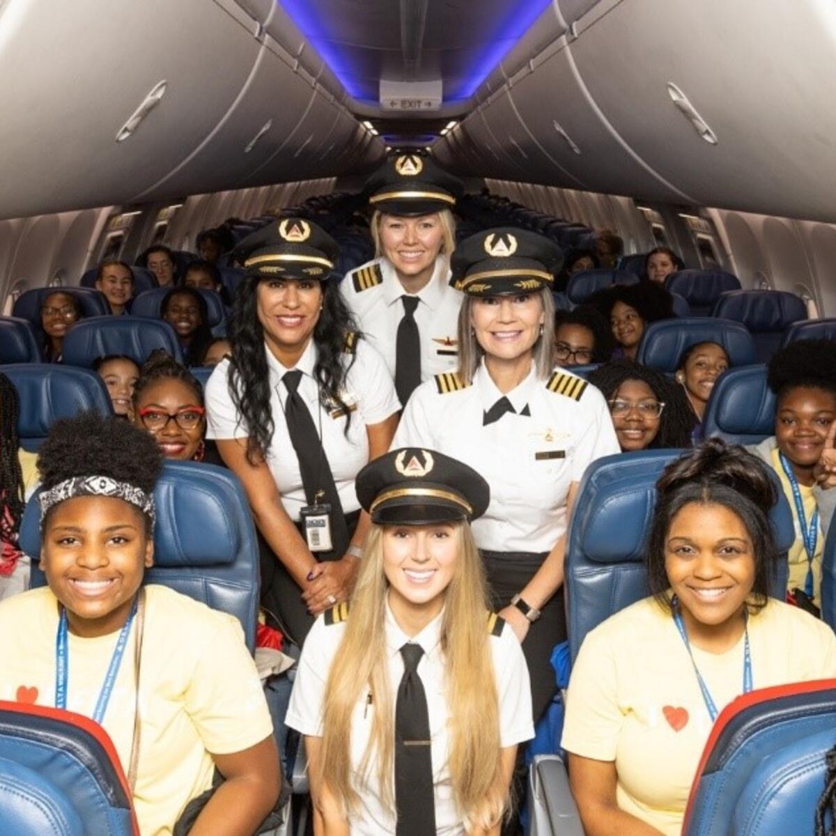 The girls selected for Delta's WING Flight 2023 pose with Delta pilots on the plane.