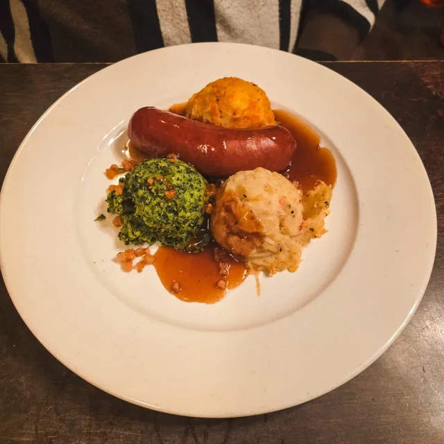 A plate with three dumplings of different flavors and a sausage, served with brown gravy.