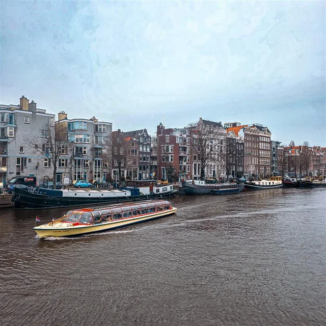 A canal boat travels along a river lined with traditional narrow buildings and moored houseboats.