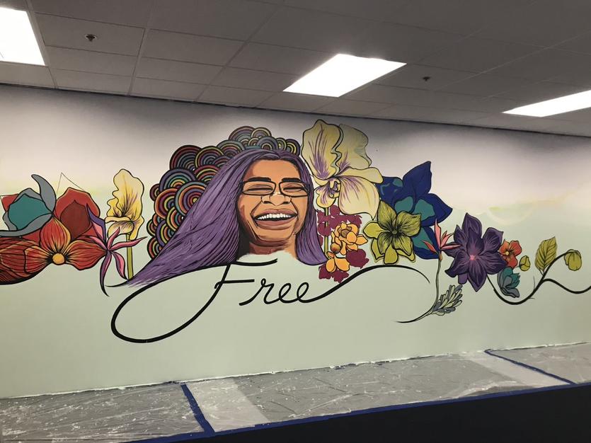 Final mural of a smiling woman on surrounded by flowers and rainbows on top of the word 'free'