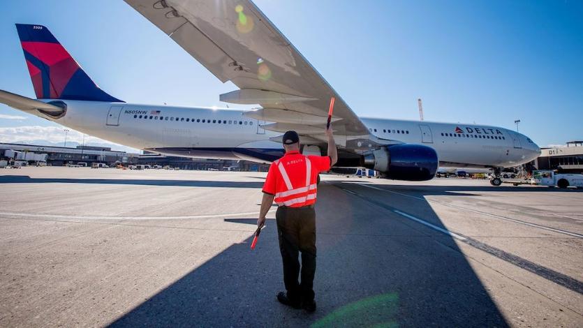 A Delta employee guides a taxiing plane.