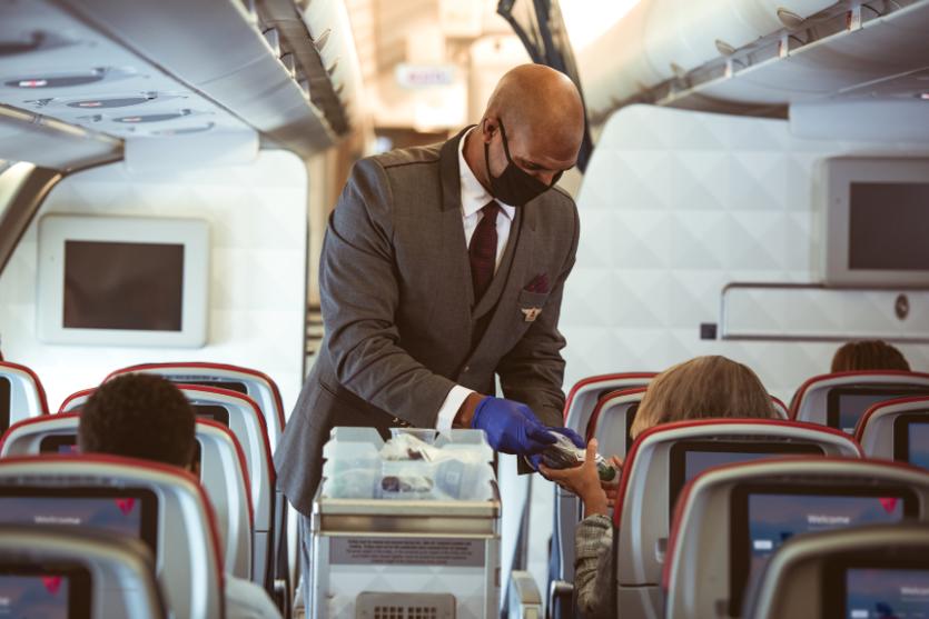 A masked flight attendant serves customers.