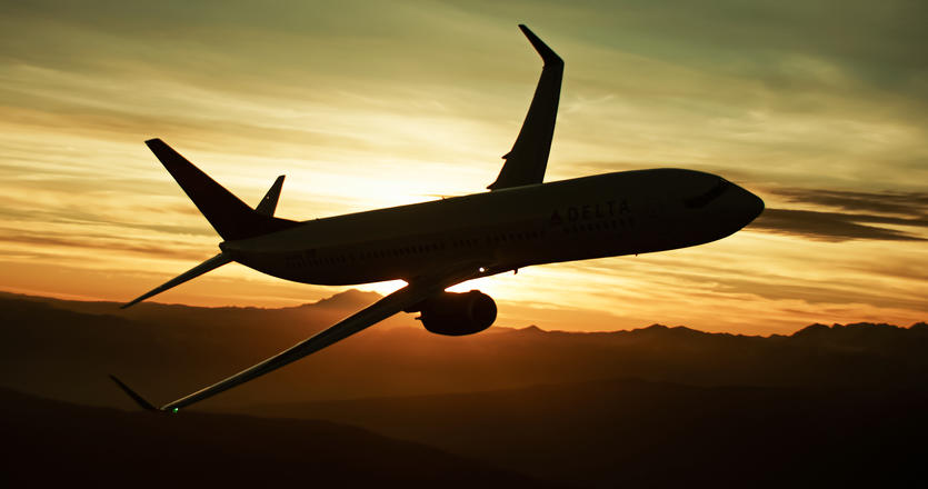 A 737-900 flies with a sunset in the background, creating a silhouette of the aircraft.