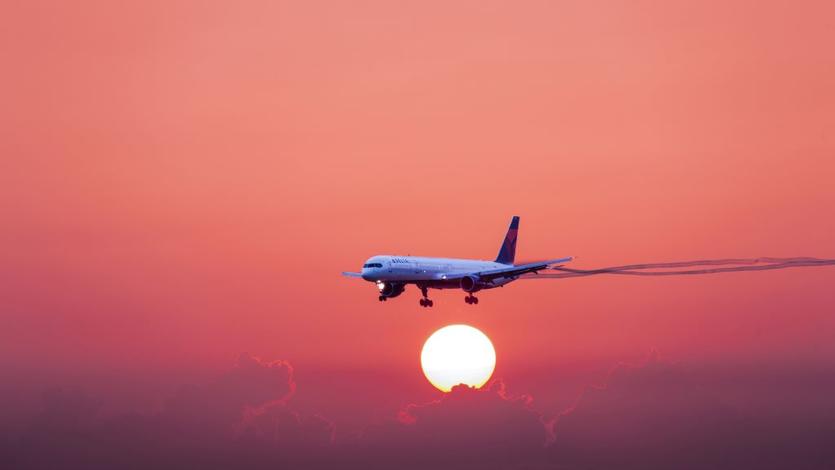 A 757-300 in flight with a red-hued sunset and cloud background.