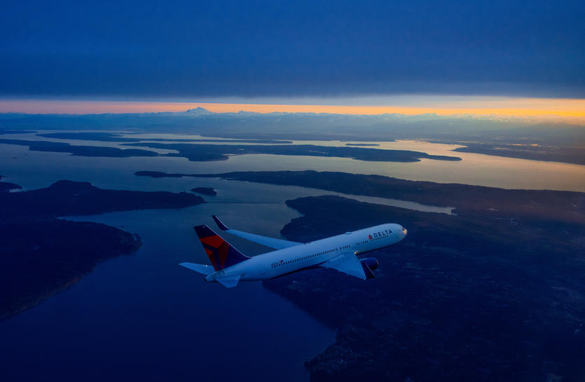 A 767-300 flies over various medium-sized bodies of water and land with a cascading night sky.