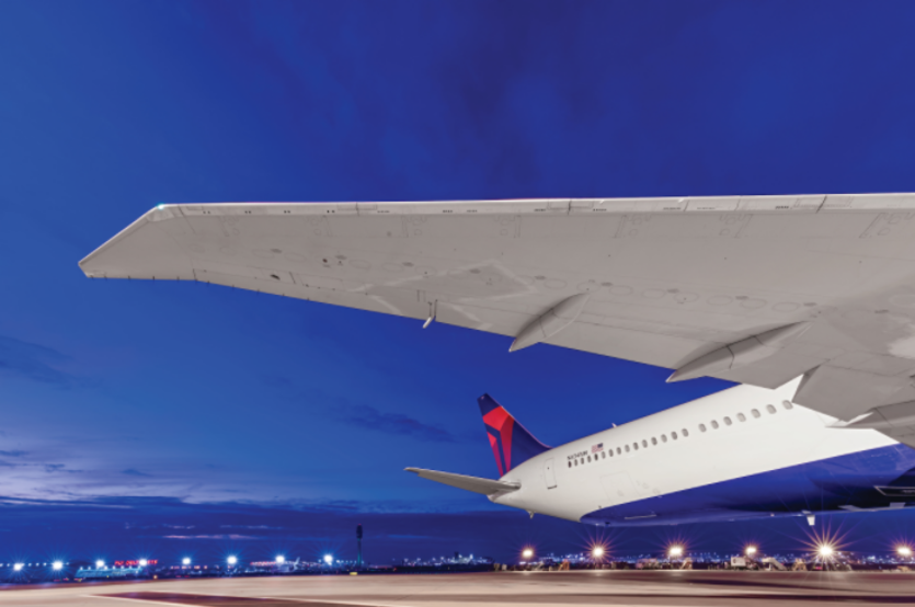 Overlooking an evening skyline lit by the runway, Delta's Boeing 767-400 dorsal area features a wingspan of 171 feet and a tail height of over 50 inches.