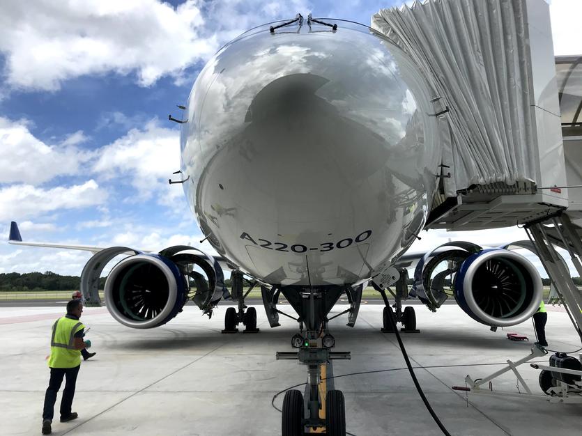 Nose of A220-300 parked on tarmac with stair truck and employees