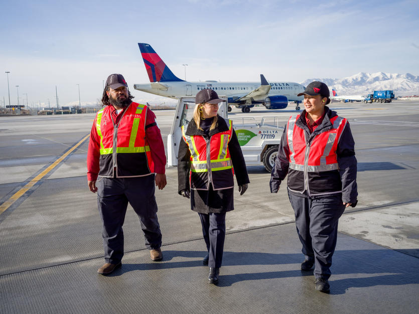 Delta Chief Sustainability Officer Pam Fletcher (middle) talks with Aircraft Load Agent Thomas Tuikolovatu (left) and Ramp Agent Sinai Pauni (right) about how they use eGSE at Salt Lake City International Airport (SLC).