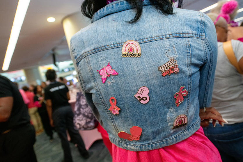 A breast cancer survivor shows off her collection of Breast Cancer Awareness pins on the back of her jean jacket.