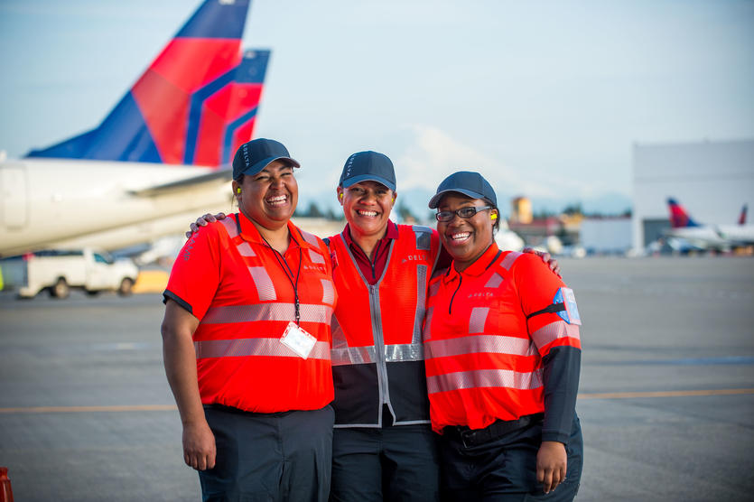 Three ramp agents stand in front of Delta aircraft at the Seattle-Tacoma International Airport.