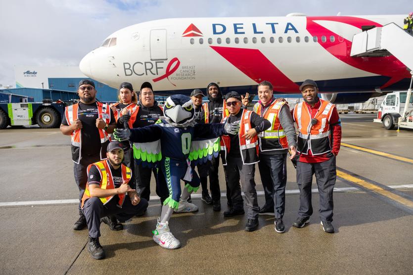 Delta ground crew members pose in front of the airline's "Pink Plane" with the Seattle Seahawks mascot.
