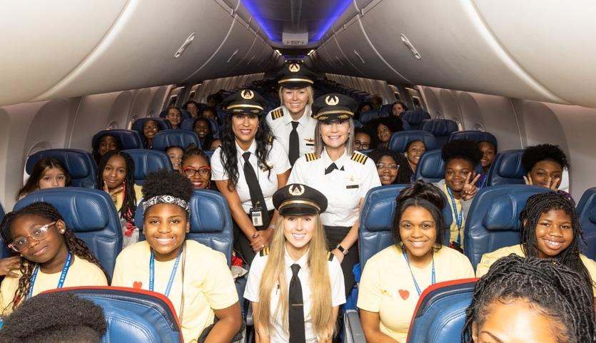 The girls selected for Delta's WING Flight 2023 pose with Delta pilots on the plane.