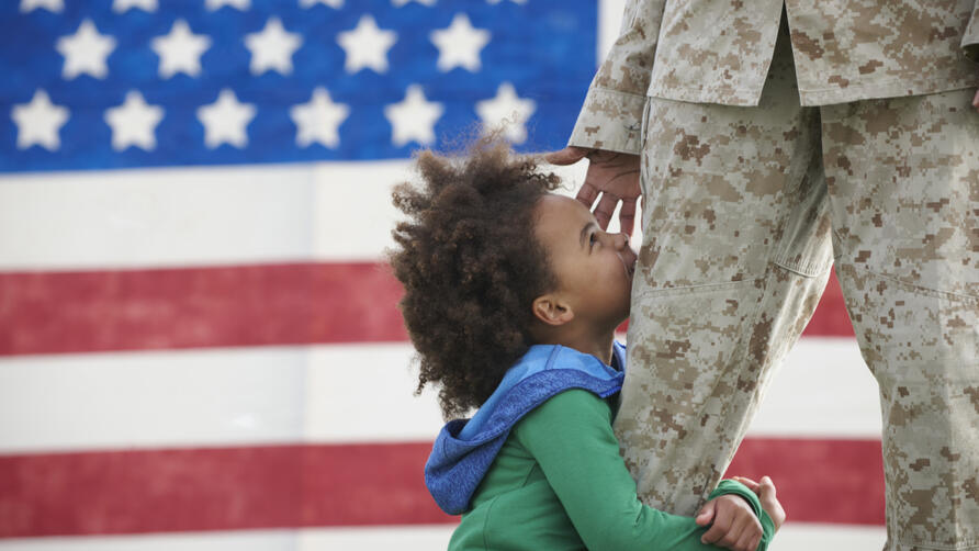 A child hugs a service member in uniform.