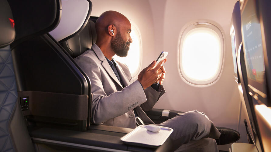 A Delta customer sits in Delta's First Class cabin, holding their phone.