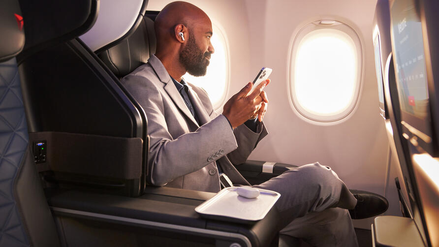 A Delta customer sits in Delta's First Class cabin, holding their phone.