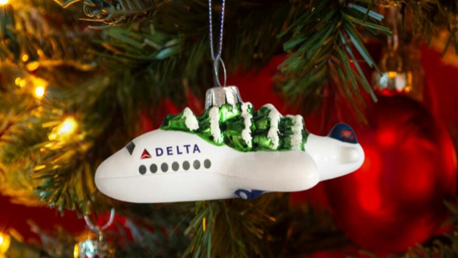 Soar into style with our Festive Delta Plane Ornament. Made of glass with a whimsical tree on top, make sure to snag one before it takes off! 