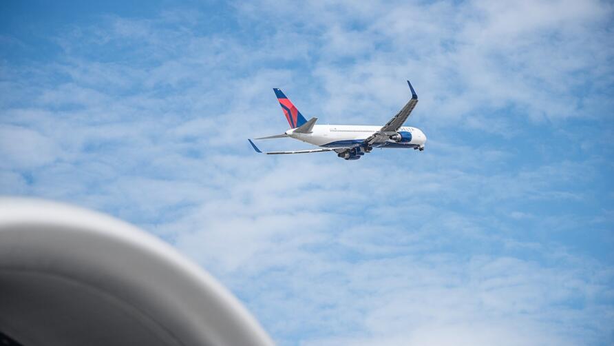 Delta 767 aircraft shortly after takeoff with blue sky and clouds in background