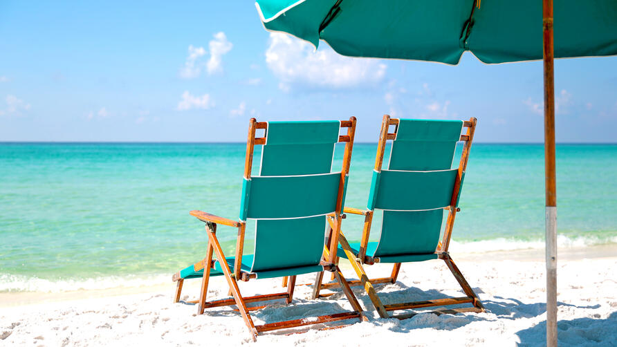 Two empty beach chairs in the sand facing turquoise blue ocean.