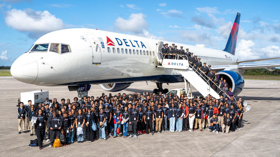 Group shot of DREAM flight attendees standing in front of Delta plane on tarmac. 