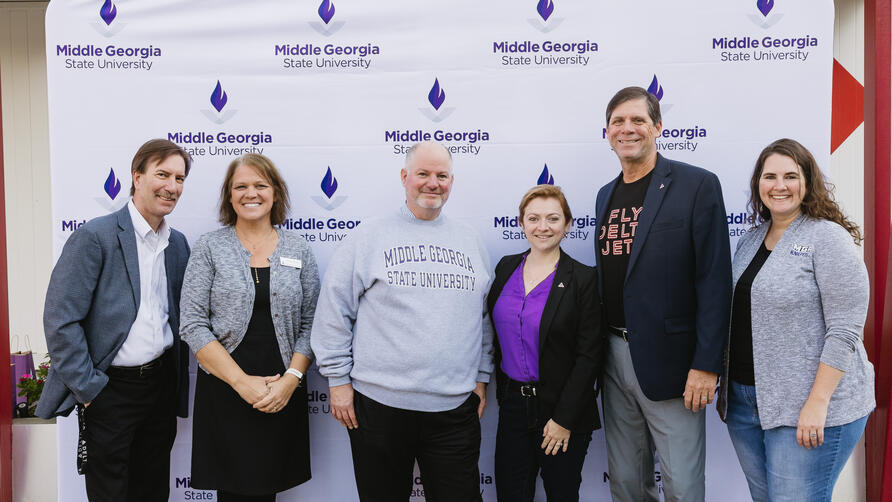 Six people standing in front of a Middle Georgia State University step-and-repeat banner, posing for a group photo.