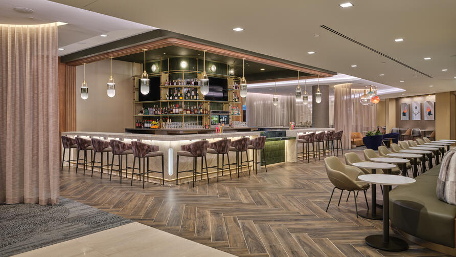 Lounge bar with high‑back stools, illuminated shelving, warm lighting and adjacent seating areas with small tables
