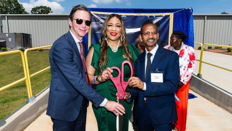 Group of individuals holding oversized ceremonial scissors at an outdoor ribbon-cutting event.