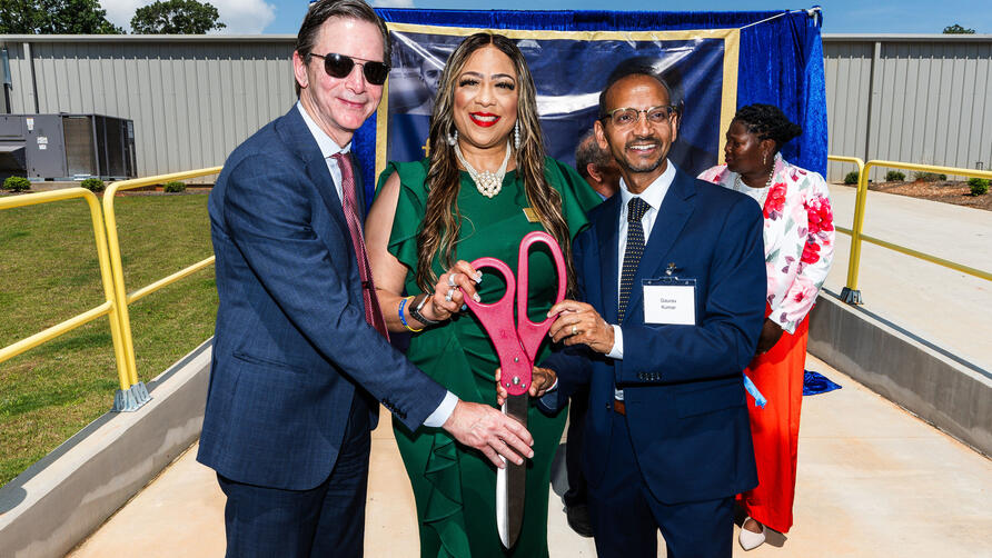 Group of individuals holding oversized ceremonial scissors at an outdoor ribbon-cutting event.