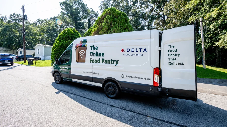 The Online Food Pantry delivery van, supported by Delta, parked in a neighborhood with its rear door open.