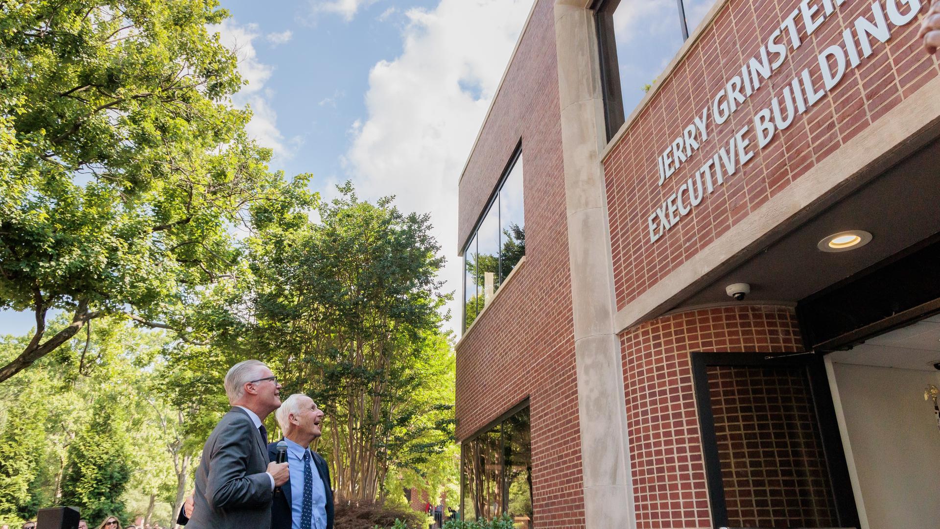 Delta CEO Ed Bastian and former Delta CEO Jerry Grinstein look up at a building.