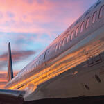 The side of a 757-200 with sunset reflected along with the tail and wing in view.