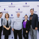 Six people standing in front of a Middle Georgia State University step-and-repeat banner, posing for a group photo.