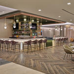 Lounge bar with high‑back stools, illuminated shelving, warm lighting and adjacent seating areas with small tables