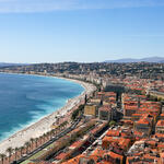Aerial view of a curved Mediterranean beach and waterfront city with red-tiled roofs.