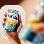 Hand holding a chilled Fresca grapefruit citrus soda can, with an airplane window softly blurred in the background.