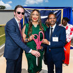 Group of individuals holding oversized ceremonial scissors at an outdoor ribbon-cutting event.