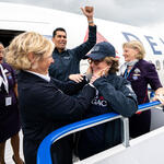 Delta employees and volunteers stand on an airport boarding ramp beside a Delta aircraft, welcoming a passenger as they exit the plane.