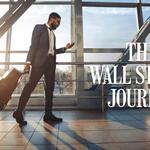Traveler in a suit walks through a sunlit airport terminal, pulling a rolling suitcase and looking at a phone, with “The Wall Street Journal” text overlaid.