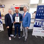 Three people pose at a Delta airport gate ceremony, with the center person holding a commemorative plaque. Banners on both sides read “Andruw Jones Gate A25,” featuring baseball-themed artwork and Delta branding.