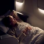  Passenger resting in a lie-flat Delta One seat with bedding, illuminated by soft cabin lighting near an aircraft window.
