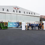 Group stands in front of Delta Air Lines’ historic hangar at the Delta Flight Museum alongside a tractor, timber load and Georgia SAF Coalition signage during a sustainable aviation fuel event.