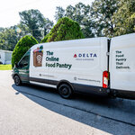 The Online Food Pantry delivery van, supported by Delta, parked in a neighborhood with its rear door open.