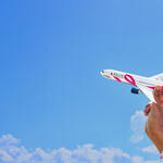 Hand holding a pink-branded Delta model airplane against a blue sky with clouds, symbolizing support for breast cancer awareness.